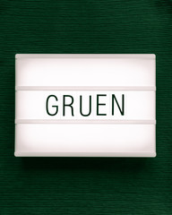 Leuchtkasten mit dem deutschen Wort "Grün" auf dunkelgrünem Hintergrund; flat lay, von oben