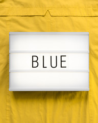 Lightbox with the word "Blue" on a sunny yellow background to express a contrast; complementary, flat lay