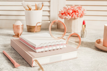 Female workspace with paper notebook, pink flowers, coffee cup, lipstick, makeup brushes and...
