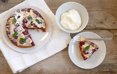Freshly baked cherry cake and whipped cream on rustic wooden planks, high angle view from above, copy space