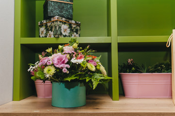 Fototapeta na wymiar Multicolored fresh decorative flowers in a green pot on a wooden shelf. Photography, concept.