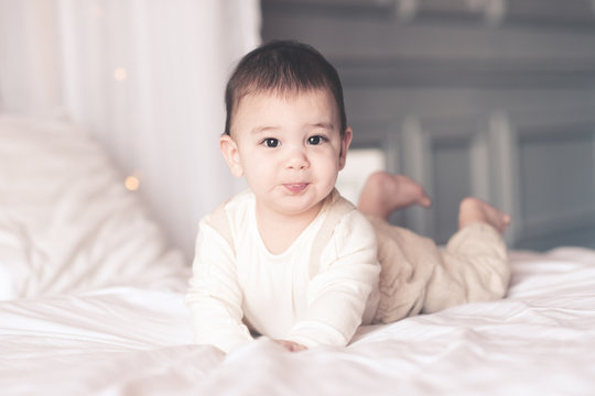 Smiling Baby Boy Under 1 Year Old Wearing Stylish Clothes Lying In Bed Closeup. Looking At Camera. Childhood.