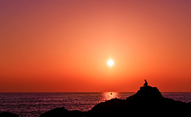 Fototapeta premium Picturesque sunset on the beach with a man sitting on a rock. North Goa, India