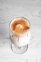 Dalgona Korean Iced Coffee, a trendy fluffy creamy whipped coffee on a white wooden table. new trends in cages