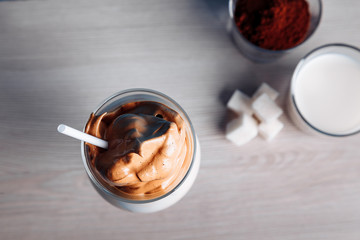 Dalgona Korean Iced Coffee, a trendy fluffy creamy whipped coffee on a white wooden table. new trends in cages
