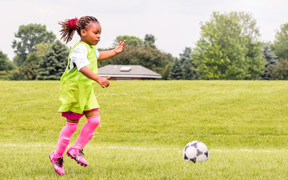 A young African American girl is learning how to play soccer on a sunny day	