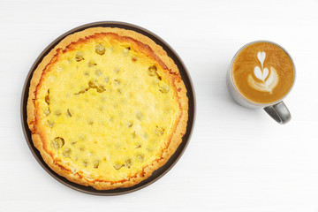 Homemade gooseberry pie with yogurt filling and cup of coffee cappuccino on white wooden table. Top view.