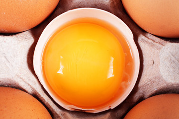Chicken eggs in a paper tray, one egg is broken