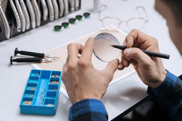 Young professional optometrist is working with lens in optical workshop using special tools and...