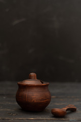Clay pot with a lid and a clay spoon. Pottery on a black background.