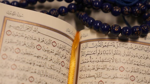 An open Quran lying on a table with a prayers bead lying on it-the shot is approaching to the Quran