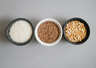 Containers of grain products, buckwheat, rice and peas in storage jars on the grey background