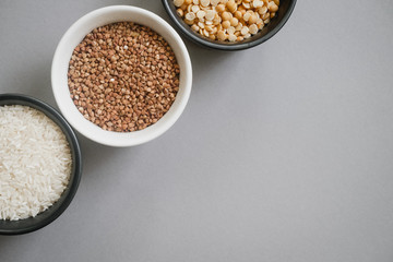 Containers of grain products, buckwheat, rice and peas in storage jars on the grey background