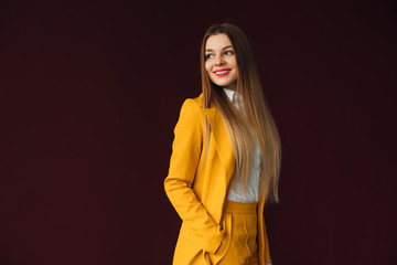 woman holds her hand in pocket of yellow suit and smile on the b