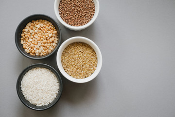 Containers of grain products, buckwheat, bulgur, rice and peas in storage jars on the grey background