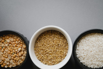 Containers of grain products, bulgur, rice and peas in storage jars on the grey background.