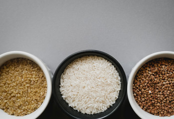 Containers of grain products, bulgur, rice and peas in storage jars on the grey background.