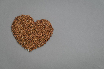 Heart-shaped uncooked buckwheat on the grey background. Healthy diet, copy space.