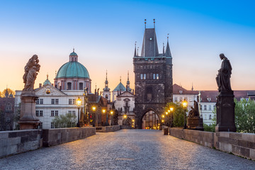 Lamps shining on the medieval stone Charles bridge with statues of saints during twilight, Prague,...