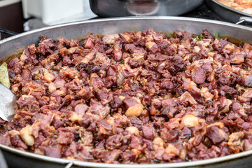 Large metallic pan with different types of deep fried meat pieces being cooked with steam, in display for sale at a street food market, photographed with selective focus
