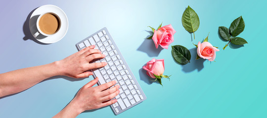 Woman using computer keyboard with pink roses - flat lay