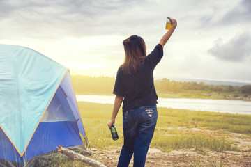 A lady traveler Camping on the river / mountain. Relaxing drink in the sunset. Campers who like to challenge and relax. The concept of camping and hiking. 