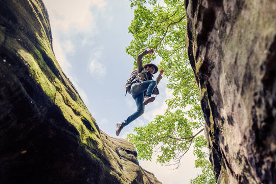 Man backpacking hiking. Make a jump over a steep cliff / valley. Activity in holiday and hiking concept. Add noise effect and film grain filter.