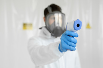 Close-up shot of doctor wearing protective respiratory mask ready to use infrared forehead thermometer gun to check body temperature for virus symptoms epidemic virus outbreak concept coronavirus