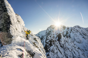 An alpinist climbing a steep ice, snow and rock face in alpine like mountain landscape of High...