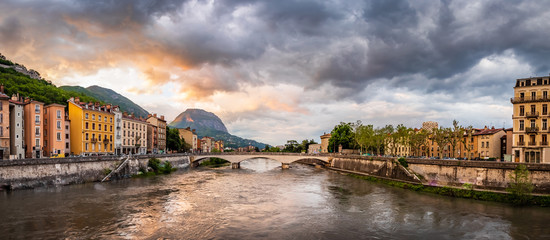 Panorama with a dramatic sunset looking down the Isere river towards a grand mountain in Grenoble France