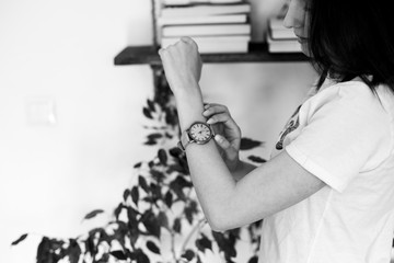 close up photo of female hand wearing yellow wrist watch  with roman numerals with bookshelf in...