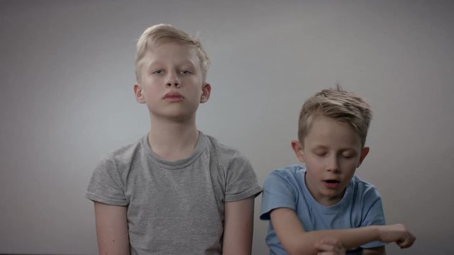 Two boys are sneezing one by one during the coronavirus epidemic. Young and old brothers catched a cold and feeling bad siiting against white background.