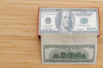 A large wad of American dollars is lying next to a wooden box