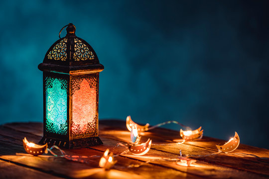 Ramadan Lantern with Colorful Light Glowing at Night and Glittering with Bokeh Lights on Ground. Festive Greeting Card, Invitation for Muslim Holy Month Ramadan Kareem. Blue Dark background