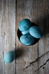 colored marble eggs lie in a cup, next to a willow branch, as a symbol of Easter, on a wooden table. rustic 