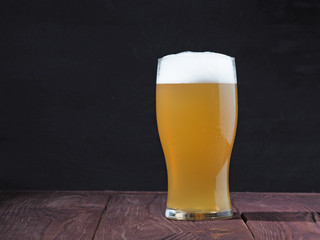 a steaming glass of unfiltered beer with a frothy cap on a wooden table against a dark background