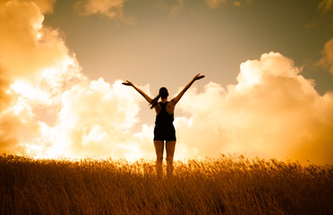 Fototapeta na wymiar Young happy woman standing in a field with arms up tot he sky feeling free and energized.