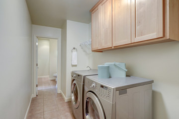 Long bright laundry room interior with washer and dryer and birch tree wood cabinets.