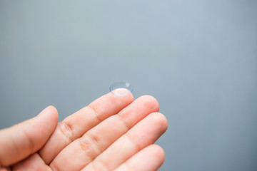 Lens on the finger. The transparent lens is on your hand. Lens on a blue background. Myopia. On a blue background with an empty space