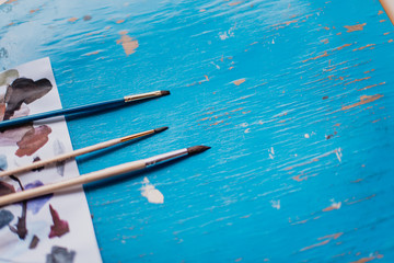 Brushes for painting on the table with a plant and a set of paints on wight and blue background