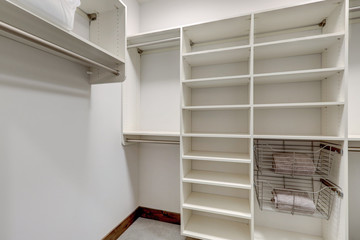 Master bedroom walk in closet with empty white shelves.