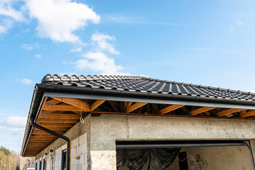 The roof of a single-family house covered with a new ceramic tile in anthracite against the blue sky, visible trusses.
