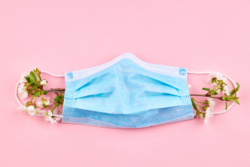 respiratory surgical face mask on a pink background decorated spring flowers. pandemic beauty concept.
