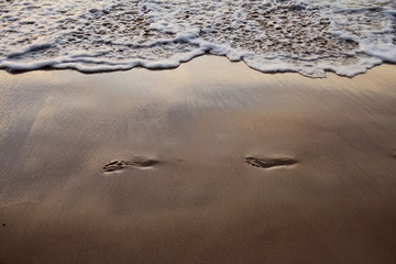footprints in the sand near the sea wave