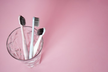 Toothbrushes in a glass on a pink background, flat lay with space for text.