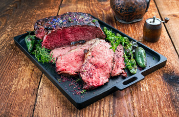 Traditional Commonwealth Sunday roast with sliced cold cuts roast beef with herbs and chili as closeup on a modern design tray
