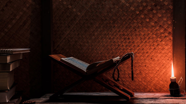 Quran and Islamic prayer beads in a rustic house room lit by traditional oil lamp. Concept of Ramadan in rural area.