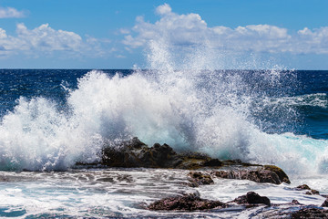 Naklejka premium Wave breaking on rock offshore Hawaii's Big Island. Deep blue pacific ocean, sky and clouds in the distance. 