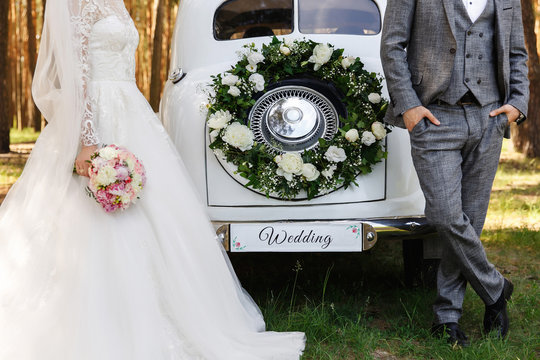 Stylish wedding couple, elegant newlyweds, groom and bride posing near white Just Married car with inscription ''Wedding''
