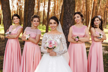 Group portrait of bridesmaids in pink dresses and bride in white wedding dress holding bouquet of...